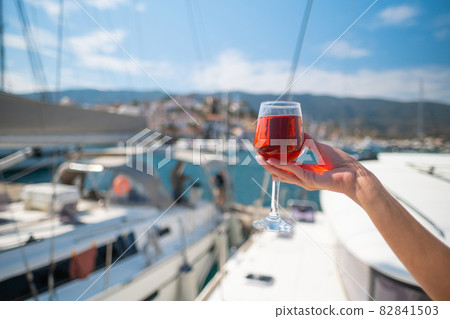 Woman holding glass of wine against yachts at the harbor of Poros. Greece Woman holding glass of wine against yachts at the harbor of Poros. Greece 82841503