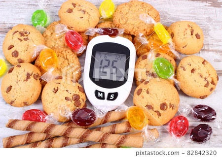 Glucometer with result sugar level and colorful candies with cookies, diabetes 82842320