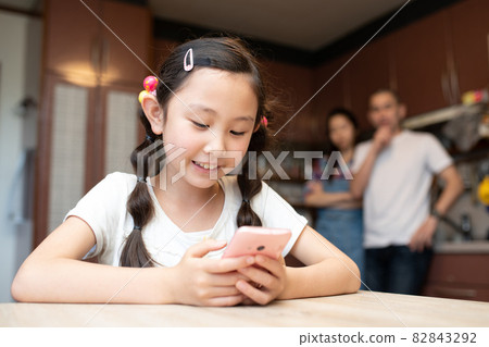A girl looking at a smartphone and her parents in trouble A girl looking at a smartphone and her parents in trouble 82843292