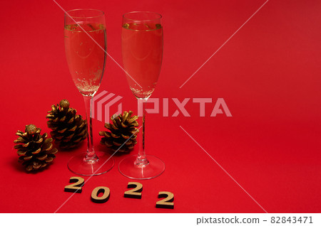 Studio shot of group of New year object, wooden 2022 numerals, golden pine cones and champagne flutes with sparkling wine isolated on red background with copy space. Merry Christmas concept 82843471