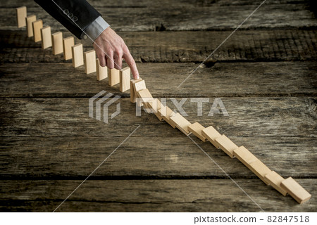 High angle view image of a businessman stopping domino effect High angle view image of a businessman stopping domino effect 82847518