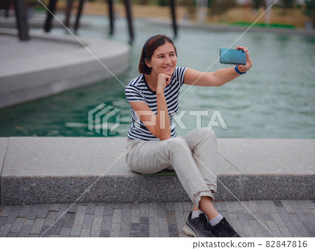 Portrait of young woman in park with smartphone Portrait of young woman in park with smartphone 82847816