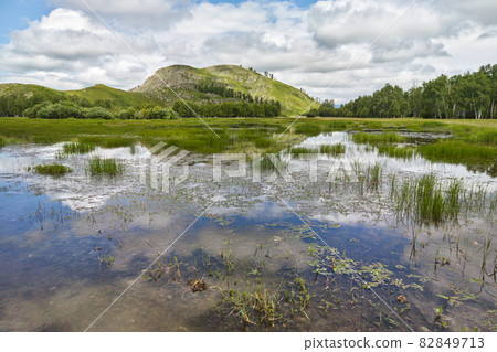 Mountain reflection in lake. Green hills. Blue sky with clouds Mountain reflection in lake. Green hills. Blue sky with clouds 82849713