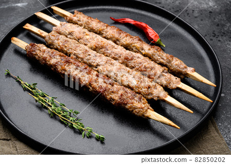 Shish kebab on a stick, from ground land mutton meat, on plate, on black dark stone table background 82850202