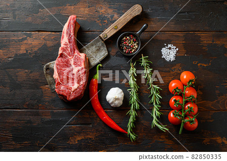 Raw Delmonico steak on meat cleaver. Organic farm marbled prime black angus beef. Dark wooden background. Top view. With seasonings, peppercorns, chilie, rosemary,salt,garlic.. 82850335