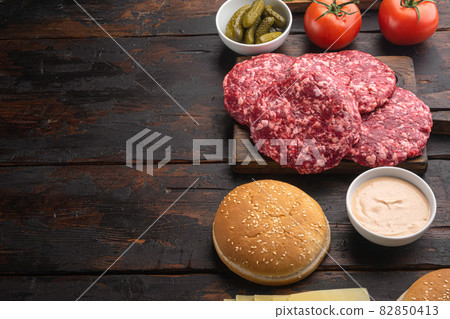 Raw Ground beef meat Burger steak cutlets and seasonings with buns, on old dark wooden table background, with copy space for text 82850413