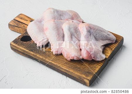 Uncooked chicken wings, on wooden cutting board, on white stone background Uncooked chicken wings, on wooden cutting board, on white stone background 82850486
