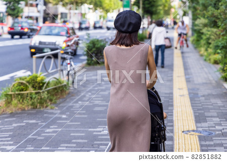 Back view of a mother wearing a black hat and pushing a baby carriage 82851882