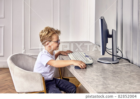 Happy european little boy in glasses sits behind computer. 82852004