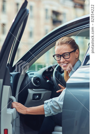 Great day. Beautiful and happy middle aged business woman in classic wear getting out of her modern car, she is arrived at work in the morning 82854222
