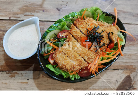 Breaded fried chicken with organic colorful salad and serving with caesar sauce on wooden table at western restaurant, food recipe menu advertisement Breaded fried chicken with organic colorful salad and serving with caesar sauce on wooden table at western restaurant, food recipe menu advertisement 82858506