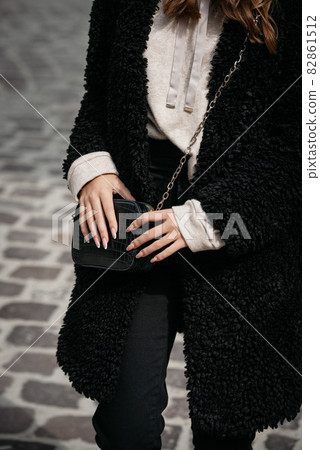 Close-up photo of young beautiful woman in black fur coat, jeanse and shoes posing on street 82861512