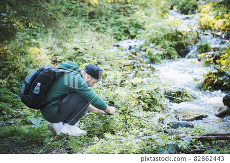 A young male tourist takes pictures on a smartphone camera in a forest. 82862443