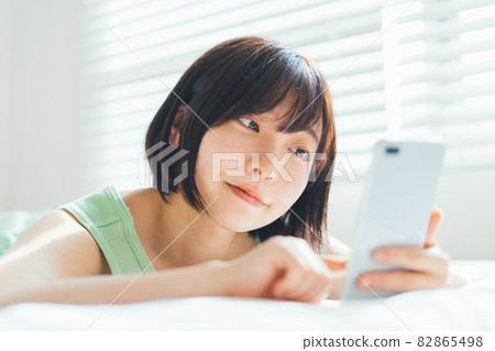A woman lying on the bed and using a smartphone A woman lying on the bed and using a smartphone 82865498