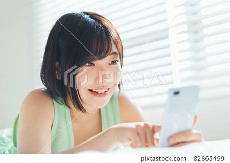 一個女人躺在床上用智能手機 82865499
