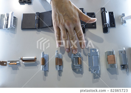 Man seller hands touching door hinges and other door hardware placed on stand Man seller hands touching door hinges and other door hardware placed on stand 82865723