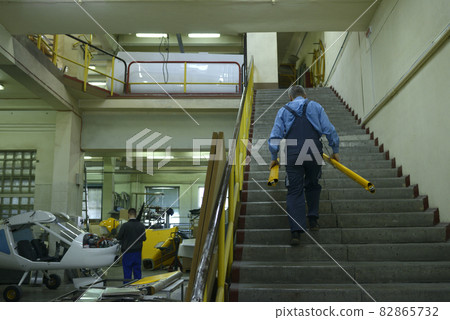 The assembly shop. Worker going up stairs carrying parts of a body plane 82865732