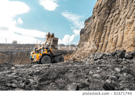 Large quarry dump truck. Big yellow mining truck at work site. Loading coal into body truck. Production useful minerals. Mining truck mining machinery to transport coal from open-pit production Large quarry dump truck. Big yellow mining truck at work site. Loading coal into body truck. Production useful minerals. Mining truck mining machinery to transport coal from open-pit production 82871740