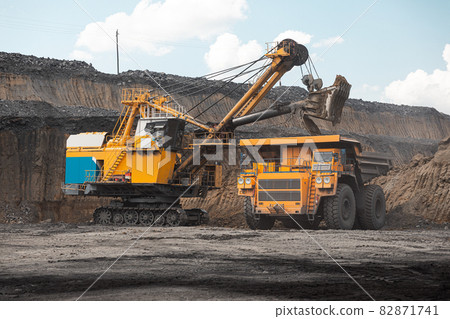 Large quarry dump truck. Big yellow mining truck at work site. Loading coal into body truck. Production useful minerals. Mining truck mining machinery to transport coal from open-pit production 82871741