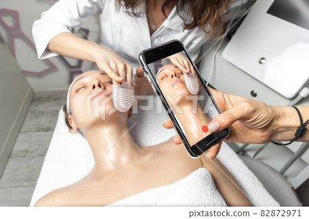 Hand holding smartphone making online live video stream of cosmetician doctor facial care procedure tutorial for online workshop master class in social media network. Remote distance learning concept 82872971