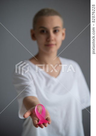 A faceless woman wearing a white t-shirt holds a pink ribbon as a symbol of breast cancer on a white background. A faceless woman wearing a white t-shirt holds a pink ribbon as a symbol of breast cancer on a white background. 82876228