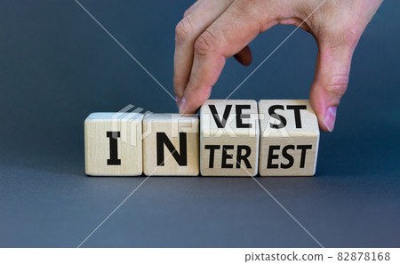 Invest or interest symbol. Businessman turns wooden cubes and changes the word 'invest' to 'interest'. Beautiful grey background, copy space. Business and invest or interest concept. 82878168