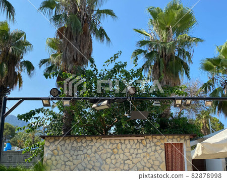 Audio visual scaffolding with concert spotlights and speakers, at an outdoor music festival, with a palm tree and blue sky in the background, and space for text on left 82878998