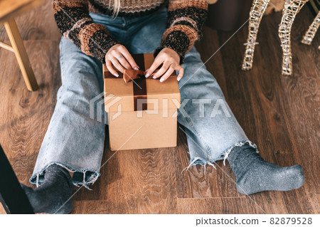 Young woman sitting on the floor and tying a bow on a Christmas present.. 82879528