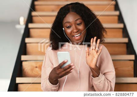 African woman having video call on smartphone sitting indoors 82880477