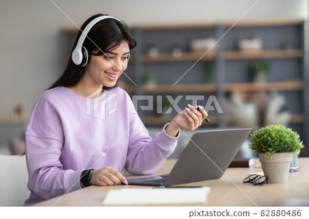 Woman in headphones having video call using laptop and talking Woman in headphones having video call using laptop and talking 82880486
