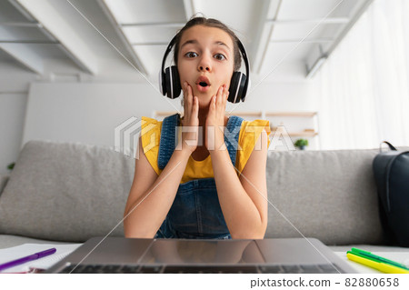 Surprised girl sitting at desk, having videocall wearing headset 82880658