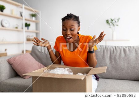 Excited black lady receiving parcel, opening cardboard box at home, satisfied with cool purchase Excited black lady receiving parcel, opening cardboard box at home, satisfied with cool purchase 82880688