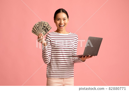 Online Lottery. Excited asian woman with dollar cash and laptop celebrating success 82880771