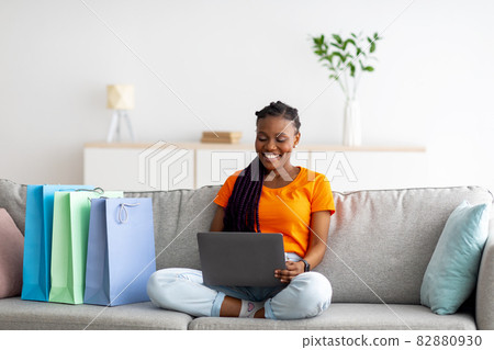 African American woman with laptop pc buying goods in internet store, sitting on sofa with shopper bags, copy space African American woman with laptop pc buying goods in internet store, sitting on sofa with shopper bags, copy space 82880930