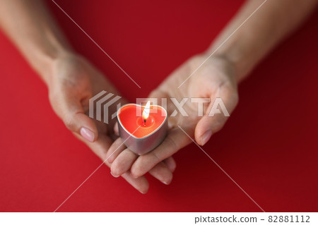 Red burning candle in the shape of a heart in female hands on red background Red burning candle in the shape of a heart in female hands on red background 82881112