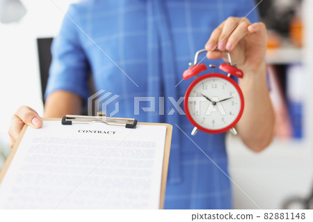 Businesswoman holds red alarm clock and contract on clipboard Businesswoman holds red alarm clock and contract on clipboard 82881148