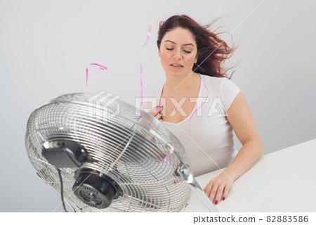 Joyful caucasian woman enjoying the wind blowing from an electric fan on a white background. 82883586