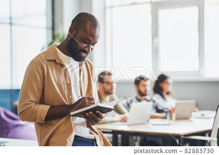 Gladsome young man writing in his note-pad Gladsome young man writing in his note-pad 82883730