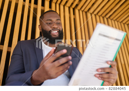 A businessman in a suit sitting on a bench with documents for analyzing in hands 82884045