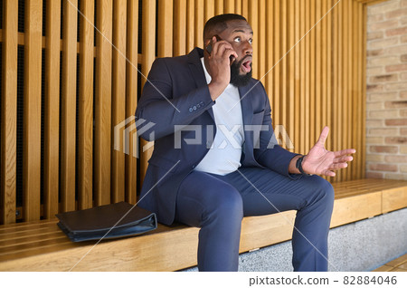 A dark-skinned businessman talking on the phone and looking involved 82884046