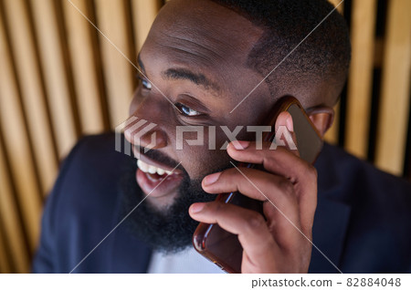A dark-skinned businessman talking on the phone and looking involved 82884048
