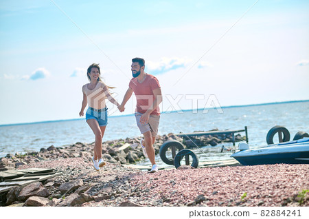 A couple holding hands and running on a beach A couple holding hands and running on a beach 82884241