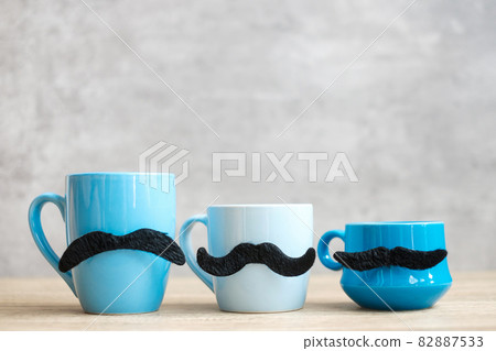 Blue coffee cup and tea mug with Black mustache decor on wood table background in the morning. Blue November, Happy Father day and International men day concept Blue coffee cup and tea mug with Black mustache decor on wood table background in the morning. Blue November, Happy Father day and International men day concept 82887533