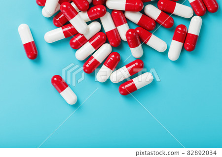 A handful of Red and white pill capsules on a blue background. Free space Top view 82892034
