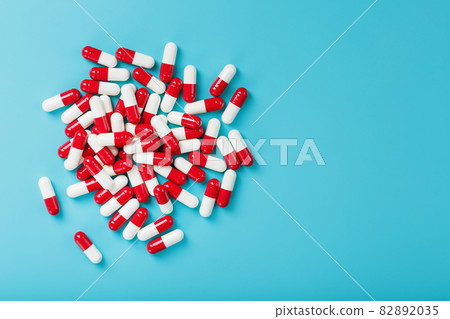 A handful of Red and white pill capsules on a blue background. Free space Top view 82892035
