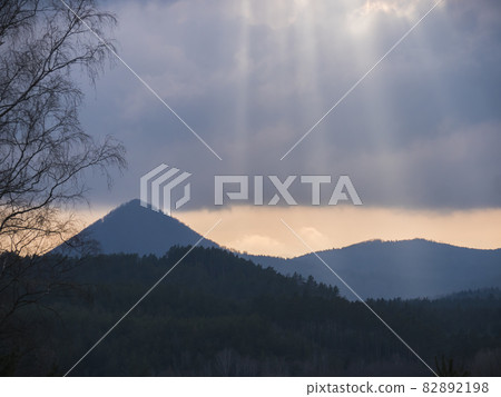 Overcast sky before sunset with sun rays at forest landscape with hill Klic, Kleis. Sunlight shining through hole of clouds to dark scene of mountain range. Moody natural background, copy space Overcast sky before sunset with sun rays at forest landscape with hill Klic, Kleis. Sunlight shining through hole of clouds to dark scene of mountain range. Moody natural background, copy space 82892198