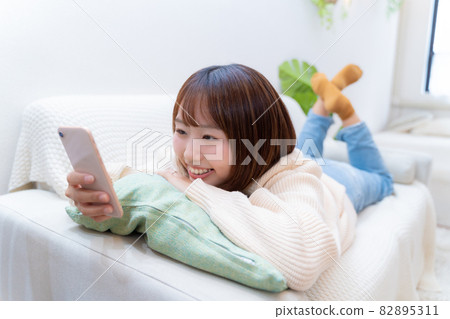 A prone woman looking at her smartphone happily A prone woman looking at her smartphone happily 82895311