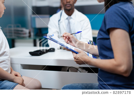 Closeup of mother writing patient information on clipboard 82897178