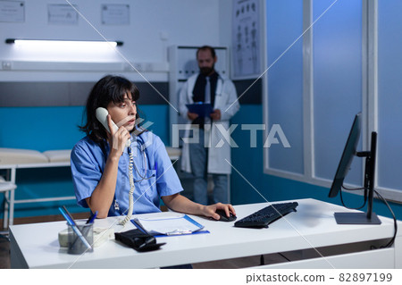 Woman nurse in uniform using landline phone for conversation 82897199