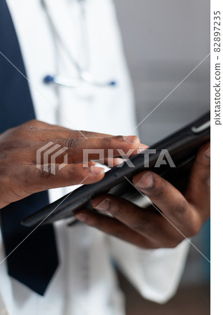 Closeup of african american doctor holding tablet computer typing healthcare treatment Closeup of african american doctor holding tablet computer typing healthcare treatment 82897235